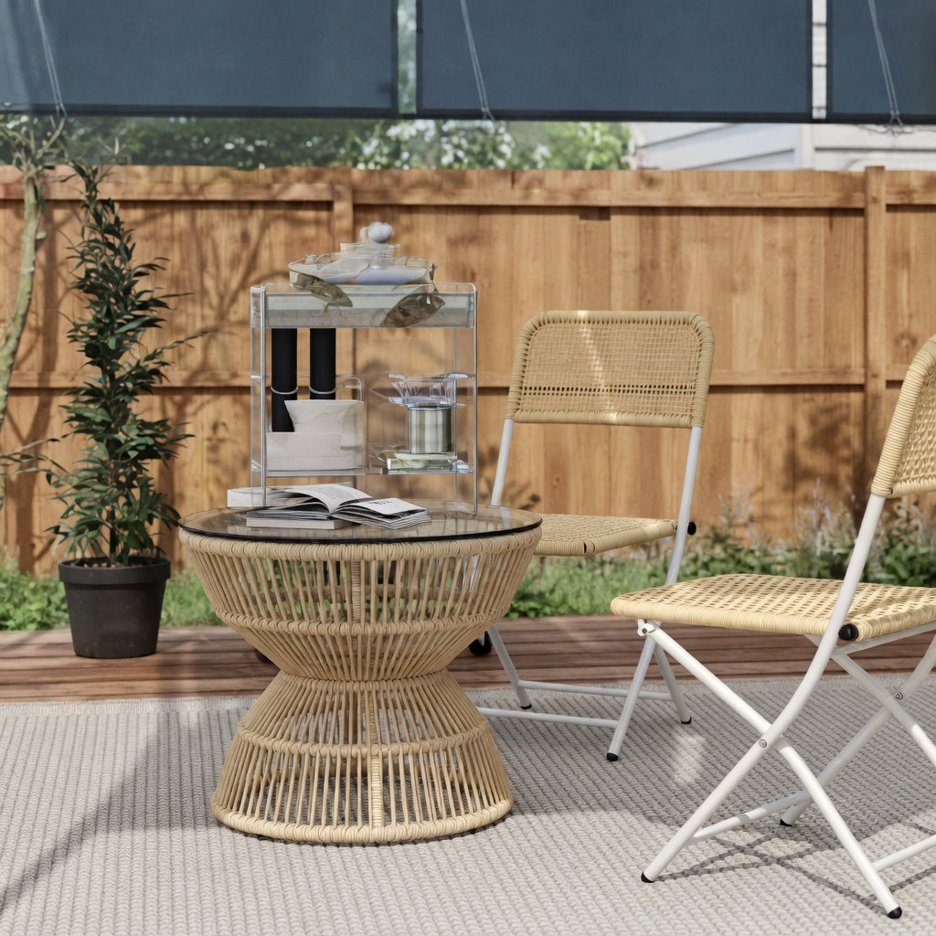 Table basse de jardin en rotin naturel avec plateau en verre posée sur une terrasse extérieure