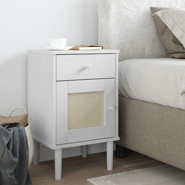 Table de chevet en bois blanc et rotin posée au bord d'un lit dans une chambre claire