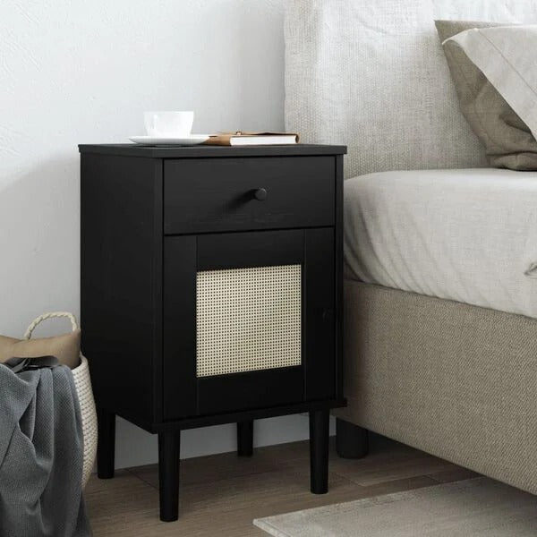 Table de chevet noire en bois et rotin posée au bord d'un lit dans une chambre claire