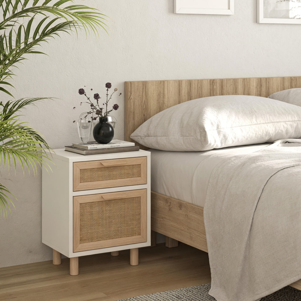 Table de chevet blanche avec tiroir et porte en rotin beige posée à côté d'un lit dans une chambre au style scandinave